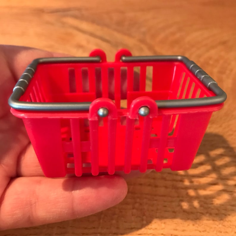 Op de afbeelding: Een klein rood plastic winkelmandje met een zilveren metalen handvat.