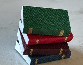 May include: A stack of four small, bound books with different colored covers. The top book is green, the second is red, the third is burgundy, and the bottom book is blue. Each book has a gold stripe along the spine.