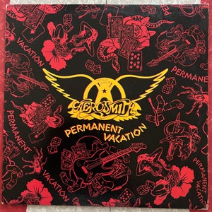 May include: A black vinyl record with a yellow and orange Aerosmith logo and the words "Permanent Vacation" in a bold font. The background is a black and red pattern with images of dice, playing cards, snakes, and flowers.