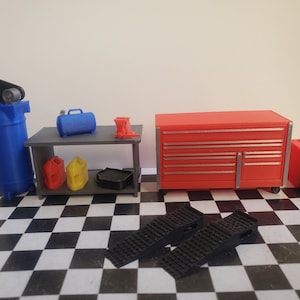 May include: A miniature garage workshop set with a red toolbox, a gray workbench, a blue air compressor, a black jack, two black ramps, and a black and gray welding machine.