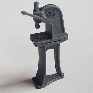 May include: A gray metal benchtop press with a lever handle and a gear. The press is labeled "No. 3".