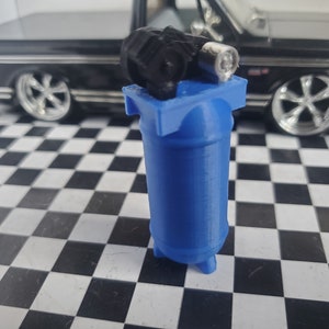 May include: A small blue air compressor with a black motor and a silver air hose. The compressor is sitting on a black and white checkered surface.