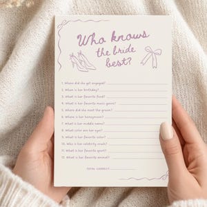 May include: A bridal shower game card with the text "Who knows the bride best?" in purple script. The card features illustrations of high heels and a bow. The card is held by a person.