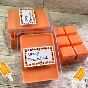 May include: Orange Dreamsicle scented wax melts in a clear plastic container. The wax melts are in both a large block and smaller cubes. The container has a label that says "Orange Dreamsicle".