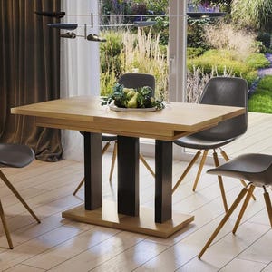 Könnte beinhalten: Ein Esstisch aus Holz mit einem schwarzen Metallgestell und vier schwarzen Stühlen. Der Tisch hat eine helle Holzoptik und die Stühle sind mit dunkelgrauem Stoff bezogen. Der Tisch ist mit einer Schale Obst in der Mitte gedeckt.