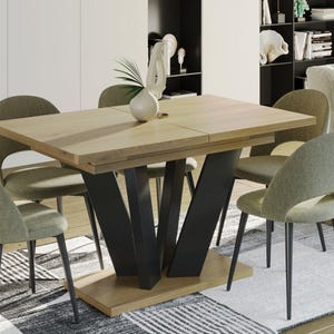 Könnte beinhalten: Ein heller Holz-Esstisch mit einem schwarzen Metallgestell und vier grünen gepolsterten Stühlen. Der Tisch hat eine Platte, die sich erweitern lässt, um ihn größer zu machen.