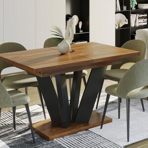 Könnte beinhalten: Ein Esstisch aus Holz mit einem schwarzen Metallgestell und vier grünen Stühlen. Der Tisch hat eine rechteckige Tischplatte und eine Einlegeplatte, die zum Vergrößern ausgezogen werden kann. Die Stühle haben eine geschwungene Rückenlehne und einen bequemen Sitz.