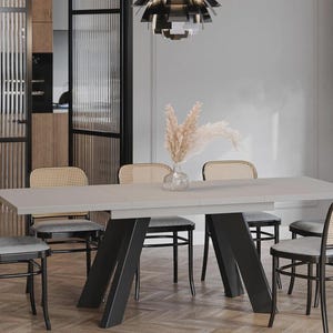 Könnte beinhalten: Ein modernes Esszimmer-Set mit einem hellgrauen rechteckigen Tisch mit schwarzen, abgewinkelten Beinen. Sechs Stühle mit grauen Kissen und gewebten Rückenlehnen umgeben den Tisch. Eine Vase mit Trockenblumen steht auf dem Tisch.