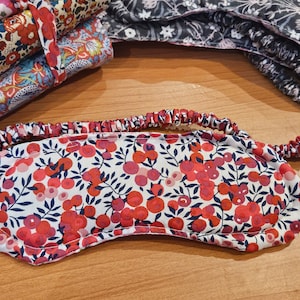 Puede incluir: Una máscara para dormir roja y blanca con un patrón floral. La máscara tiene una banda elástica para un ajuste cómodo.