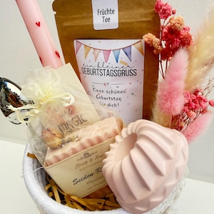 Könnte beinhalten: Ein Geschenk-Korb mit einer rosa Kerze mit roten Herzen, einem Teebeutel "Früchte Tee" und einer Karte mit der Aufschrift "ein kleiner GEBURTSTAGSGRUSS". Er enthält auch rosa Seife, Trockenblumen und einen dekorativen rosa Gegenstand.