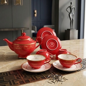Puede incluir: Un juego de té rojo que incluye una tetera, cuatro tazas y cuatro platillos. Cada pieza está decorada con patrones de filigrana dorada y detalles interiores en blanco. La tetera tiene tapa y asa curva, mientras que las tazas descansan sobre platillos.