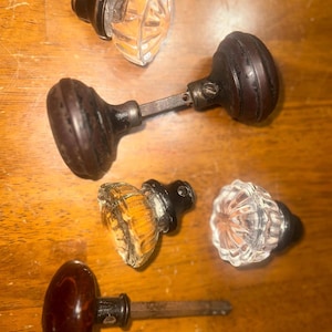May include: Five antique door knobs with a variety of styles. Two are made of dark wood, two are clear glass, and one is amber glass.