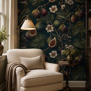 Peut inclure: Un fauteuil rembourré de couleur crème avec un coussin rectangulaire assorti et une couverture en tricot marron drapée. Le fauteuil est placé contre un mur sombre recouvert d'un papier peint au motif répétitif de figues et de fleurs blanches.