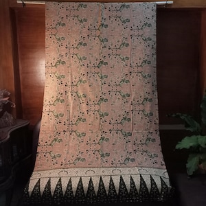 May include: A pink and green patterned fabric with a black and white border. The fabric has a traditional Indonesian batik design.