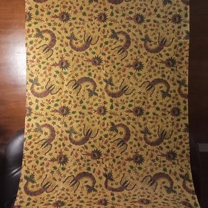 Op de afbeelding: Een gele stof met een herhalend patroon van donkergroene, rode en zwarte gestileerde bloemmotieven. De stof heeft een subtiele glans.