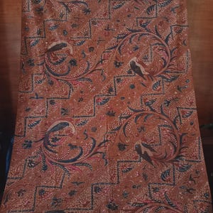 Könnte beinhalten: Ein brauner Stoff mit einem sich wiederholenden Muster aus stilisierten Vögeln und floralen Designs. Der Stoff hat eine dunkelblaue und rote Farbgebung.