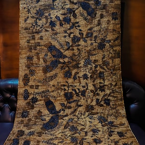 Könnte beinhalten: Ein rechteckiges Textil mit einem dichten Batikmuster in Braun- und Dunkelblautönen. Das Design zeigt komplexe florale Motive, belaubte Zweige und stilisierte Vogelfiguren, die über die gesamte Oberfläche des Stoffes verteilt sind.
