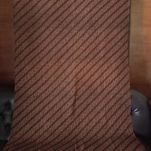 Peut inclure: Un tissu marron avec un motif à rayures diagonales. Les rayures sont composées de petits points de couleur claire sur un fond marron plus foncé. Le tissu est drapé sur une surface sombre.