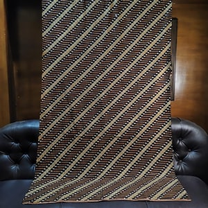 Puede incluir: Un tejido rectangular que presenta un patrón diagonal repetitivo de rayas de color marrón oscuro y negro, intercaladas con finas líneas onduladas de color claro. La tela muestra un diseño geométrico consistente en toda su superficie.