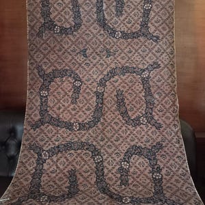 Könnte beinhalten: Ein brauner Stoff mit einem sich wiederholenden Muster aus schwarzen floralen Designs. Der Stoff hat einen Hintergrund mit Diamantenmuster.