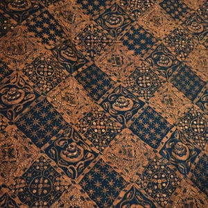 May include: A patterned textile featuring a repeating design of geometric shapes and floral motifs in navy blue and brown. The design includes squares and diamonds filled with stars and other decorative elements.
