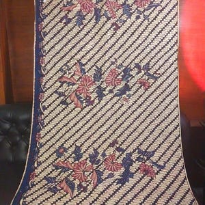 Könnte beinhalten: Ein weißer Stoff mit einem diagonalen Muster in Blau und Schwarz und rosafarbenen Blumendesigns. Der Stoff hat einen blauen Rand.