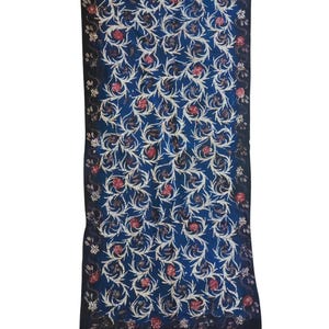 May include: A rectangular, dark blue textile with a repeating floral pattern in white and red. The design features swirling vines and flowers. The bottom edge has a decorative border with white and red triangular shapes.
