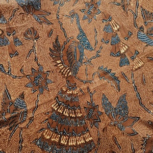 Op de afbeelding: Bruine stof met een herhaald patroon van gestileerde vogels, bloemen en bladeren in bruin- en blauwtinten. Het ontwerp heeft ingewikkelde details en een gestippelde achtergrond, waardoor een textuur ontstaat. Dit textiel is geschikt voor diverse knutselprojecten.
