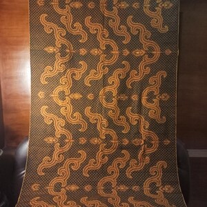Op de afbeelding: Een donkergroene stof met een herhalend patroon van gouden swirls en stippen. De stof is geweven en heeft een textuur.
