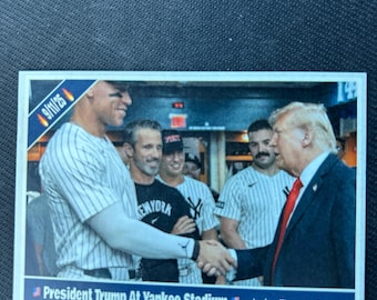May include: A baseball card featuring President Trump shaking hands with a New York Yankees player. The card has the text "President Trump At Yankee Stadium" and "Judge Ties Joe D". The date "9/11/25" is also visible.