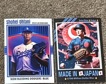 May include: Two baseball trading cards featuring Shohei Ohtani. The first card shows Ohtani in a blue and white Los Angeles Dodgers uniform with the text "2024 LA DODGERS" and "NOW BLEEDING DODGERS BLUE". The second card shows Ohtani in a blue and white baseball uniform with the text "MADE IN JAPAN" and "$700 Million Dollar Man".