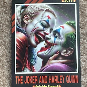 May include: A rectangular card featuring a vibrant illustration of The Joker and Harley Quinn from Suicide Squad. The Joker has green hair and the Harley Quinn has blonde hair with pigtails. The card has the year 2016 printed on it.