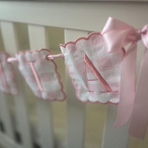 Puede incluir: Una pancarta de beb&eacute; de vichy rosa y blanco con las letras "TIA" bordadas en rosa. La pancarta est&aacute; enhebrada con una cinta rosa.