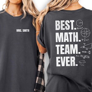 Könnte beinhalten: Dunkelgraue T-Shirts mit weißem Text. Ein Shirt trägt die Aufschrift "MRS. SMITH" auf der Vorderseite. Das andere Shirt trägt auf der Rückseite "BEST. MATH. TEAM. EVER." mit mathematischen Symbolen. Ein tolles Geschenk für Mathelehrer.
