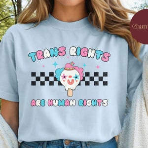May include: Light blue t-shirt with a graphic of a cartoon ice cream cone with a clown face and the text "Trans Rights Are Human Rights".