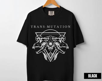 May include: Black t-shirt with the word "TRANS-MUTATION" above a white graphic of animal skulls and geometric shapes. The shirt is hanging on a wooden hanger.
