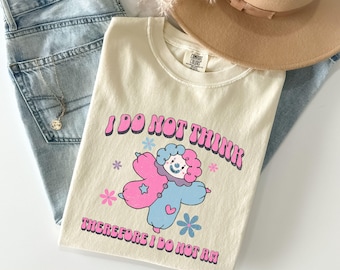 May include: A cream-colored t-shirt with a pink and blue cartoon clown and the text "I do not think therefore I do not am".