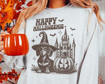 May include: A grey sweatshirt with a graphic print of a dachshund wearing a witch's hat, a castle, and a pumpkin. The text "Happy Halloweenie" is printed on the shirt.