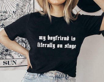 May include: Black t-shirt with the text "my boyfriend is literally on stage" in white gothic font.