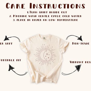 May include: Cream-colored t-shirt with a celestial design featuring a crescent moon and stars. The shirt includes care instructions: turn inside out, machine wash cold, and tumble dry low. Additional text highlights the shirt's features: super soft, non-toxic ink, comfortable fit, and vibrant design.