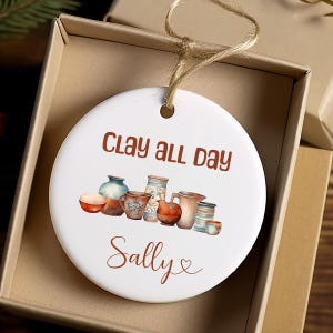 Pu&ograve; includere: Ciondolo in ceramica bianca con un'illustrazione marrone e bianca di ceramiche e il testo "Clay all day Sally".