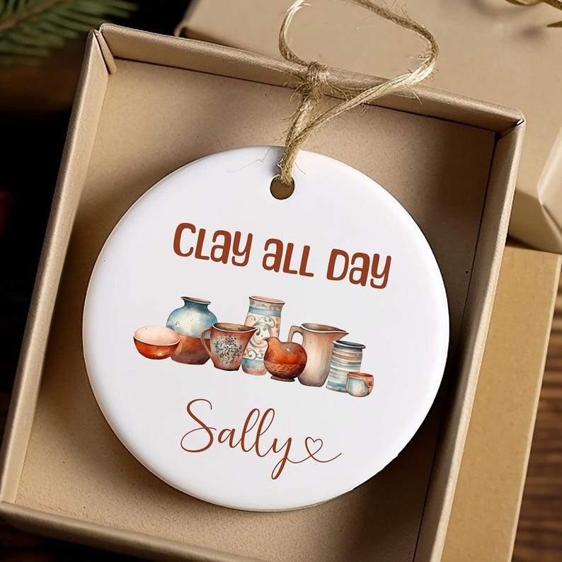Pu&ograve; includere: Ciondolo in ceramica bianca con un'illustrazione marrone e bianca di ceramiche e il testo "Clay all day Sally".