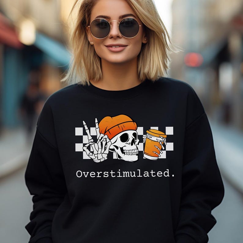 May include: Black sweatshirt with a graphic featuring a skull wearing an orange beanie, a peace sign, and a beer mug. The text "Overstimulated" is printed below the graphic.
