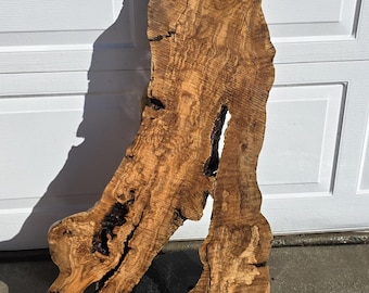 May include: A large, irregularly shaped piece of wood with a natural, brown and tan wood grain pattern. The wood has a unique, organic shape and is mounted on a black base.