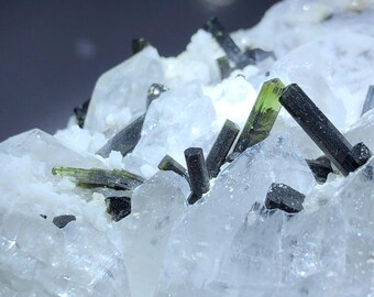 May include: A close-up shot of a mineral specimen. It features clear quartz crystals and dark green and black tourmaline crystals. The crystals are clustered together, creating a textured display. The lighting highlights the natural beauty of the minerals.