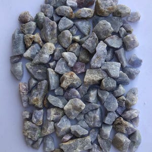 May include: A collection of small, irregularly shaped stones in shades of gray, lavender, and brown. The stones vary in size and texture, creating a natural, organic appearance. Ideal for decorative purposes or crafts.
