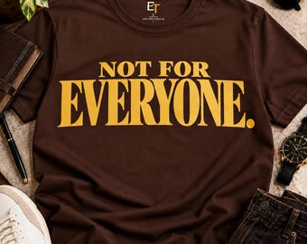 Può includere: Una t-shirt a maniche corte color marrone scuro con la scritta NOT FOR EVERYONE in grandi lettere maiuscole gialle e in grassetto sul petto. Il capo presenta uno scollo rotondo e un piccolo logo del marchio stampato all'interno del colletto.