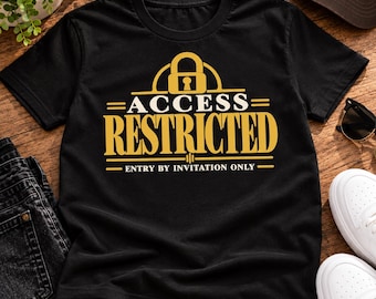 Può includere: Una t-shirt nera a maniche corte con una stampa grafica dorata di un lucchetto sopra il testo ACCESS RESTRICTED e il testo più piccolo ENTRY BY INVITATION ONLY, centrato sul petto con linee orizzontali che incorniciano la scritta.