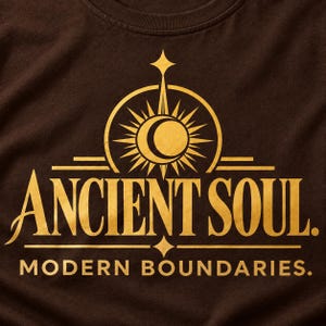 Op de afbeelding: Een donkerbruin t-shirt met een gouden grafische print. Het ontwerp bevat een centraal zon- en maansikkelpictogram boven de tekst ANCIENT SOUL. Daaronder staat de tekst MODERN BOUNDARIES. gedrukt in een strak, hoofdletterrijk lettertype.