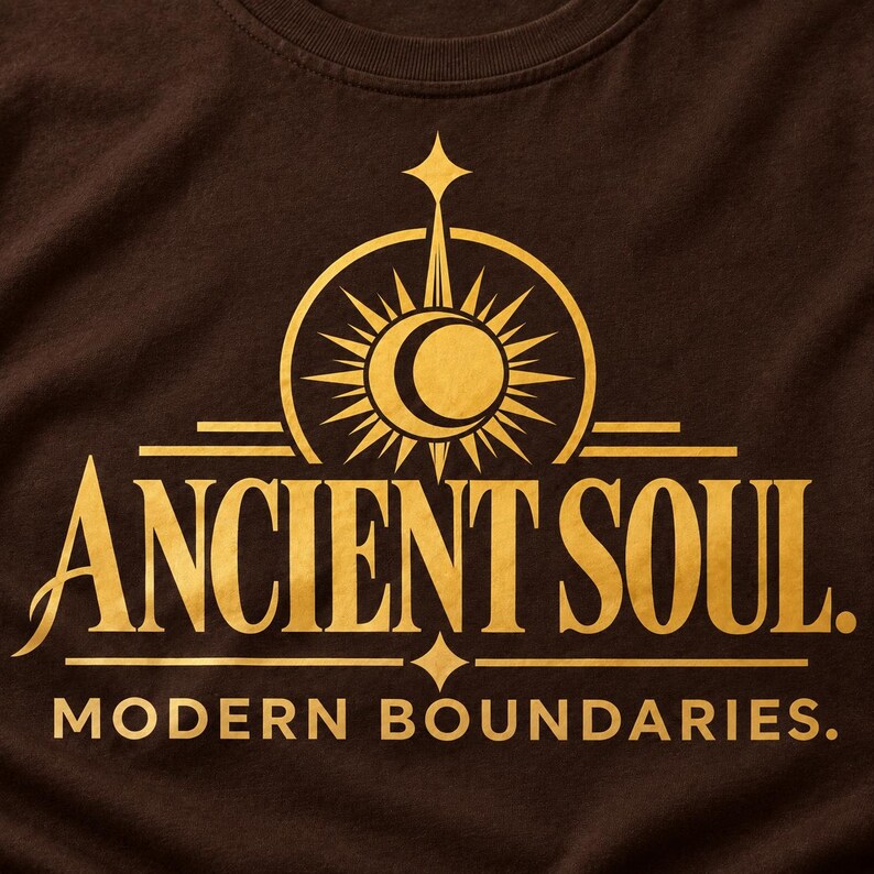 Op de afbeelding: Een donkerbruin t-shirt met een gouden grafische print. Het ontwerp bevat een centraal zon- en maansikkelpictogram boven de tekst ANCIENT SOUL. Daaronder staat de tekst MODERN BOUNDARIES. gedrukt in een strak, hoofdletterrijk lettertype.